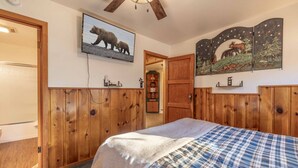 Un dormitorio con paneles de madera, una cama con manta escocesa, un televisor en la pared y un panel decorativo con un oso y árboles.