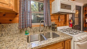 Una cocina con encimeras de granito, un lavaplatos de acero inoxidable, un microondas blanco y una estufa a gas.