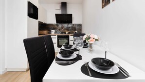 A modern dining area with a white table set for two, black plates, and a vase with flowers.