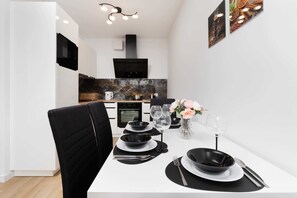 A modern dining area with a white table set for two, black plates, and a vase with flowers. - Comfortable Apartment in Downtown Gdynia | Near the Beach | Parking (Gdynia)