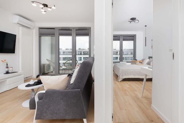 A modern apartment with a grey sofa, a small white table, a TV, and a balcony with a view of buildings. - Comfortable Apartment in Downtown Gdynia | Near the Beach | Parking (Gdynia)