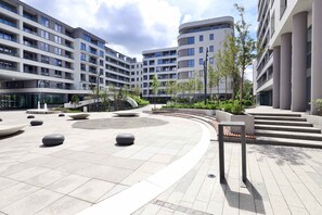 Une place urbaine moderne dotée d’un cheminement sinueux, d’espaces aménagés pour s’asseoir et d’un bâtiment comportant de nombreux balcons.