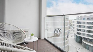 A balcony with wicker chairs, a small table with a plant, and a view of modern buildings.