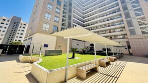 A modern building with a covered outdoor area, featuring a grassy lawn and seating benches. - A839 - A spacious apartment with garage, air conditioning and pool (Villajoyosa)