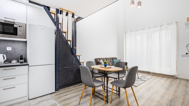 A modern kitchen with a built-in microwave, a staircase, and a dining area with a table and chairs. - Venus Apartments - Westside Residence (Budapest)