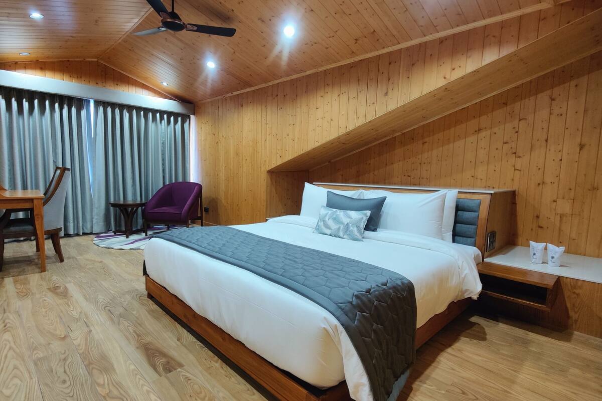 Un dormitorio con paneles de madera, una cama, un escritorio, una silla y un ventilador de techo.