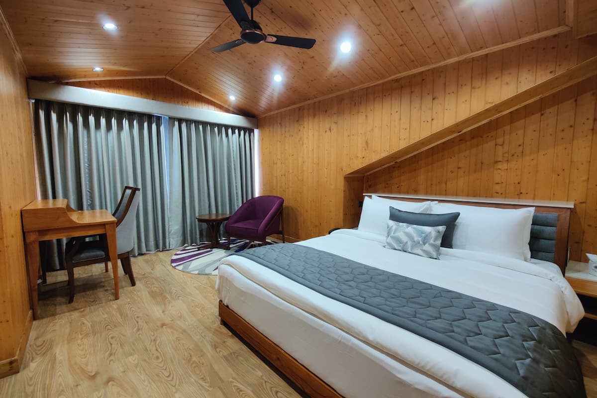 Una habitación con paneles de madera, con una cama, un escritorio, una silla y un ventilador de techo.