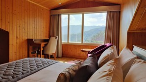 A wooden room with a bed, a desk, and a chair. There is a window with a view of mountains. - Kaithal Resort - Kasauli (Kasauli)