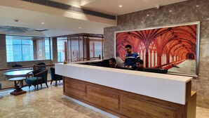 A modern reception area with a wooden reception desk, a large abstract mural, and a seating area with tables and chairs. - Kaithal Resort - Kasauli (Kasauli)