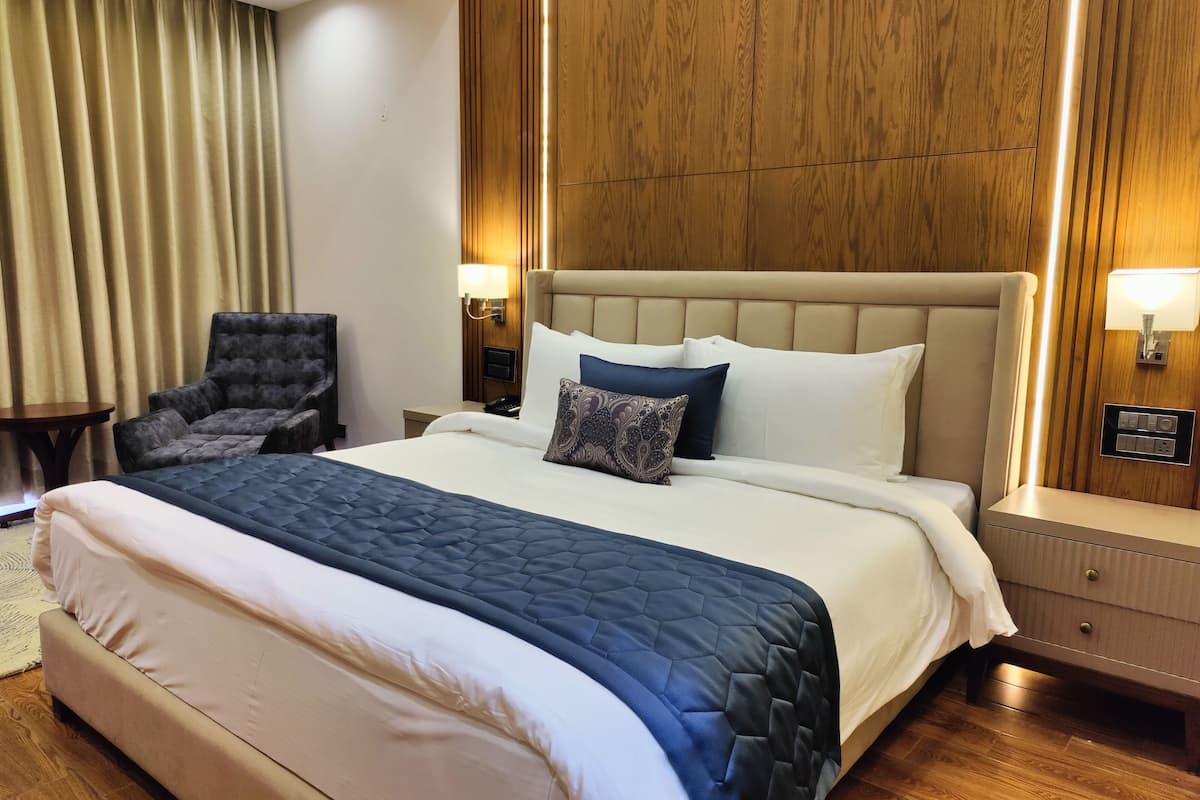Habitación de hotel con una cama grande, una silla, una mesita de noche y un panel de pared de madera.