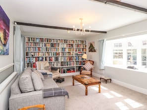 A cozy living room with a large bookshelf, a sofa, a coffee table, and a window with a view.