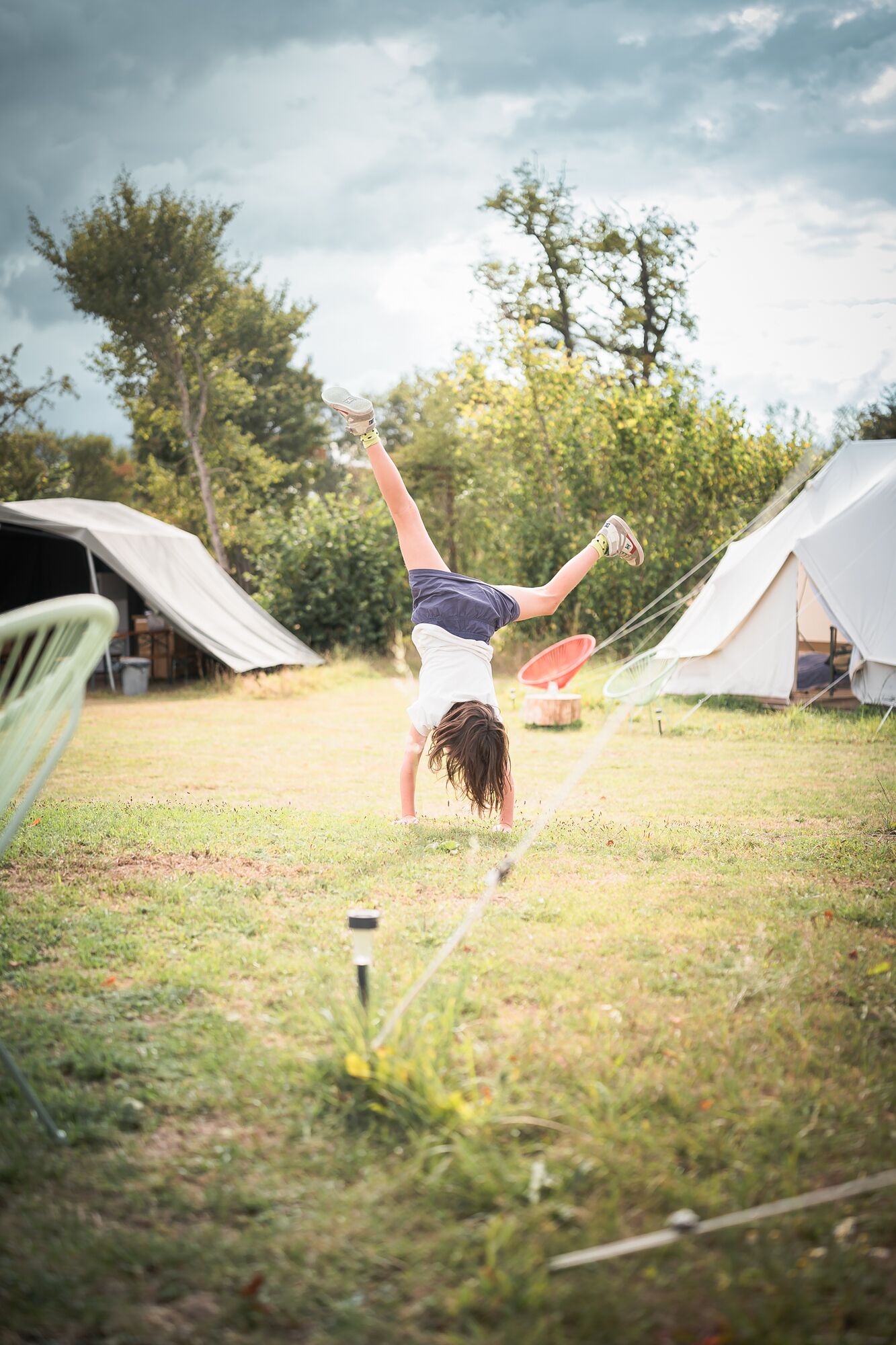 A person performing a handstand in a grassy area with tents in the background.