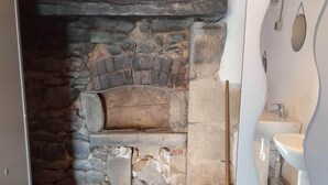 Een stenen openhaard met een rustieke uitstraling, een moderne badkamer met een wit wastafelmeubel en spiegel, en een betonnen vloer.