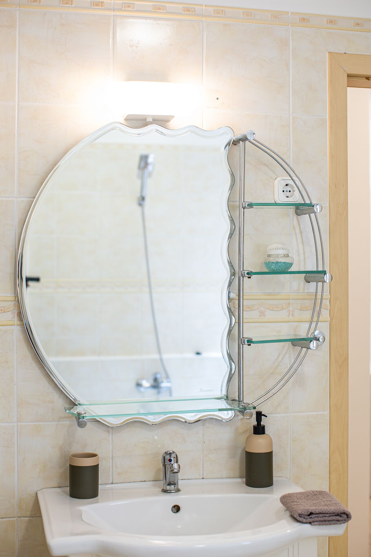 A bathroom with a round mirror, a sink, and a glass shelf with toiletries.