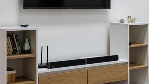 Una sala de estar moderna con una televisión de pantalla plana montada en la pared, estanterías de madera, una consola blanca y un tapete estampado.
