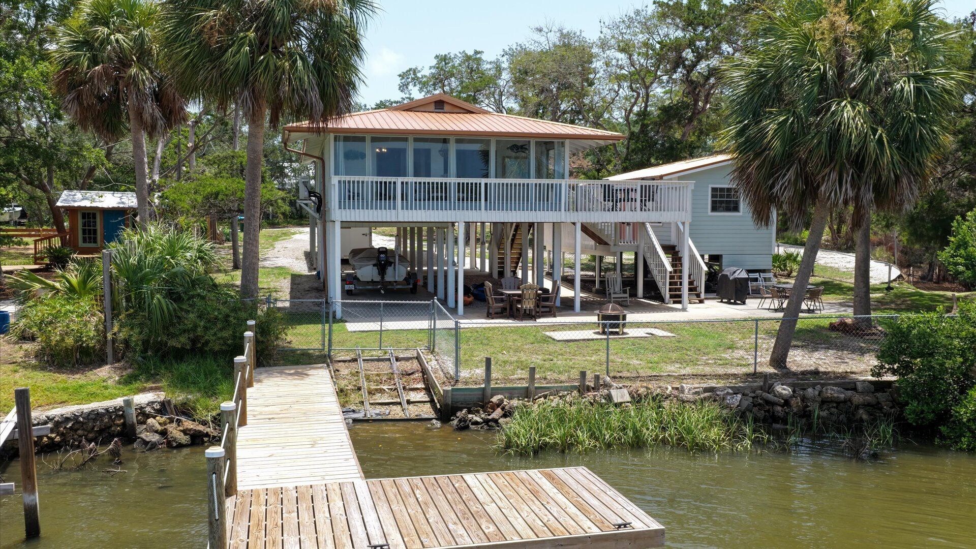 A two-story house with a covered deck and a dock extending into a body of water.