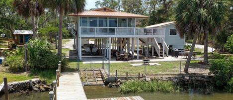 A two-story house with a covered deck and a dock extending into a body of water.