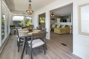 A dining area with a wooden table and chairs, a chandelier, and a view of the outdoors. - Waterfront Cottages with Sunsets, Kayaks Included! (Cedar Key)