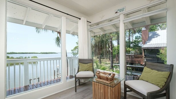 Un balcon avec deux chaises et une petite table, donnant sur une étendue d’eau et sur de la verdure.