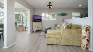 Un salon spacieux avec un canapé de couleur claire, un téléviseur et un tableau décoratif représentant des poissons.