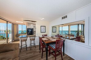 Een eetruimte met een grote tafel en stoelen, een keuken achtergrond en een balkon met uitzicht op het water.