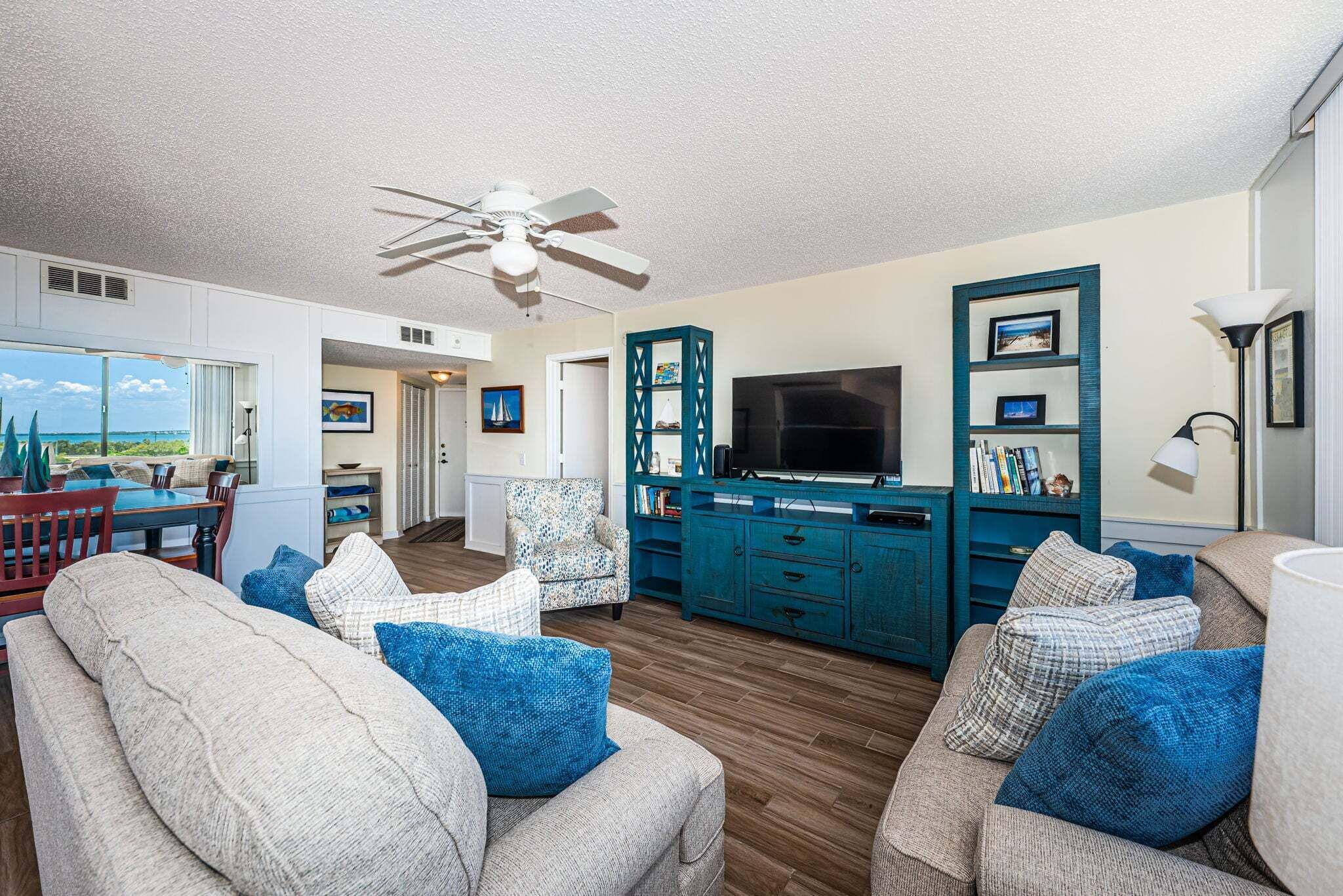 A spacious living room with a large TV, teal cabinets, and a ceiling fan.