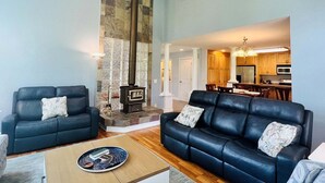 A living room with a fireplace, two sofas, a coffee table, and a dining area with a kitchen in the background.