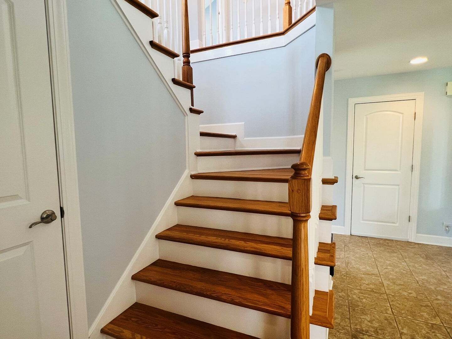 Un escalier en bois, avec des murs blancs et une porte en bas.