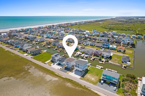 An aerial view of a coastal residential area with houses, a marina, and a beach.