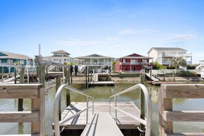 A pier leading to a marina with boats, wooden walkways, and beachfront houses.