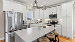 A modern kitchen with white cabinetry, stainless steel appliances, a marble island, and woven stools.