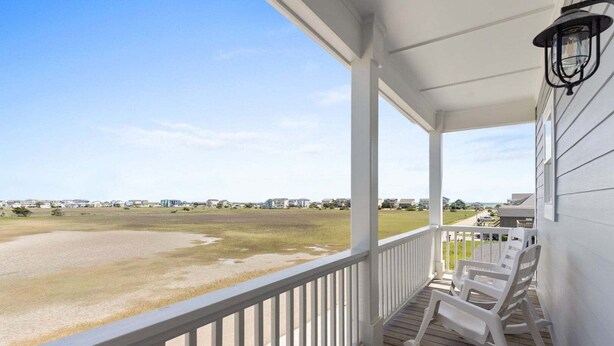 A porch with a view of a beach and houses in the distance.