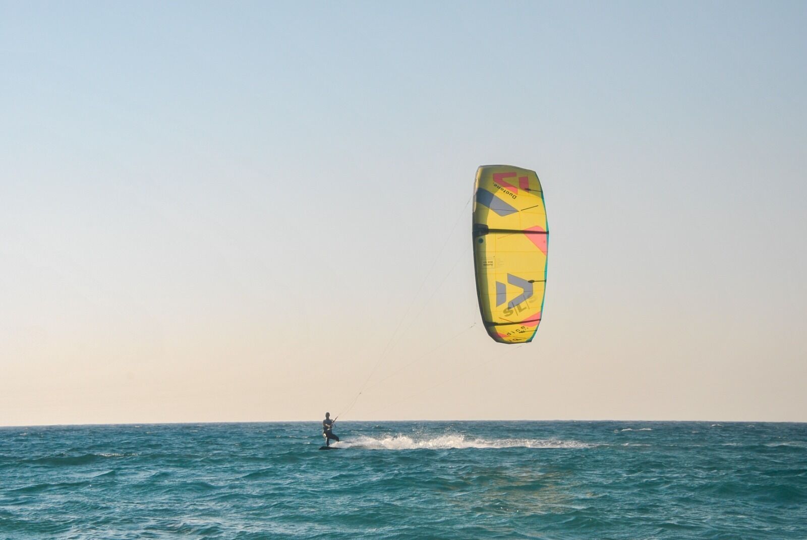 Uma pessoa praticando kitesurf no oceano, com uma pipa colorida no ar.