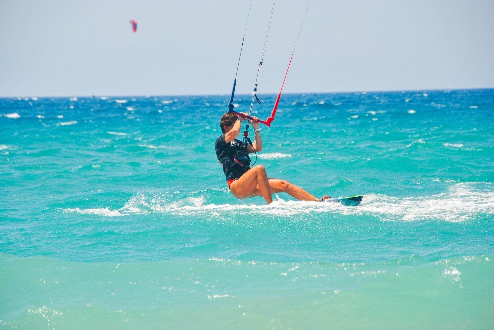 Una persona practica windsurf sobre aigües turqueses.