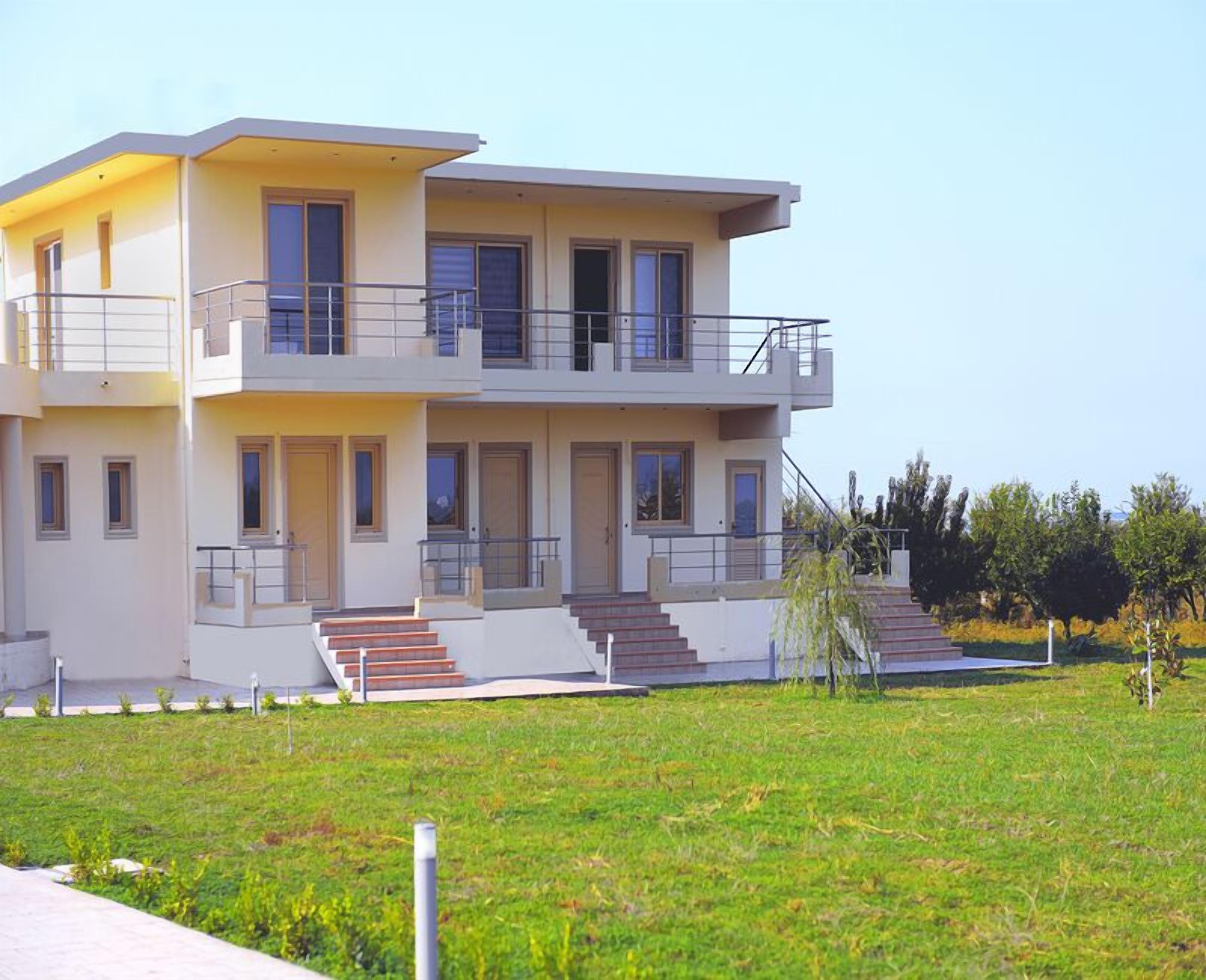 Una casa moderna de dos pisos con techo plano, ventanas amplias y un balcón en el nivel superior.