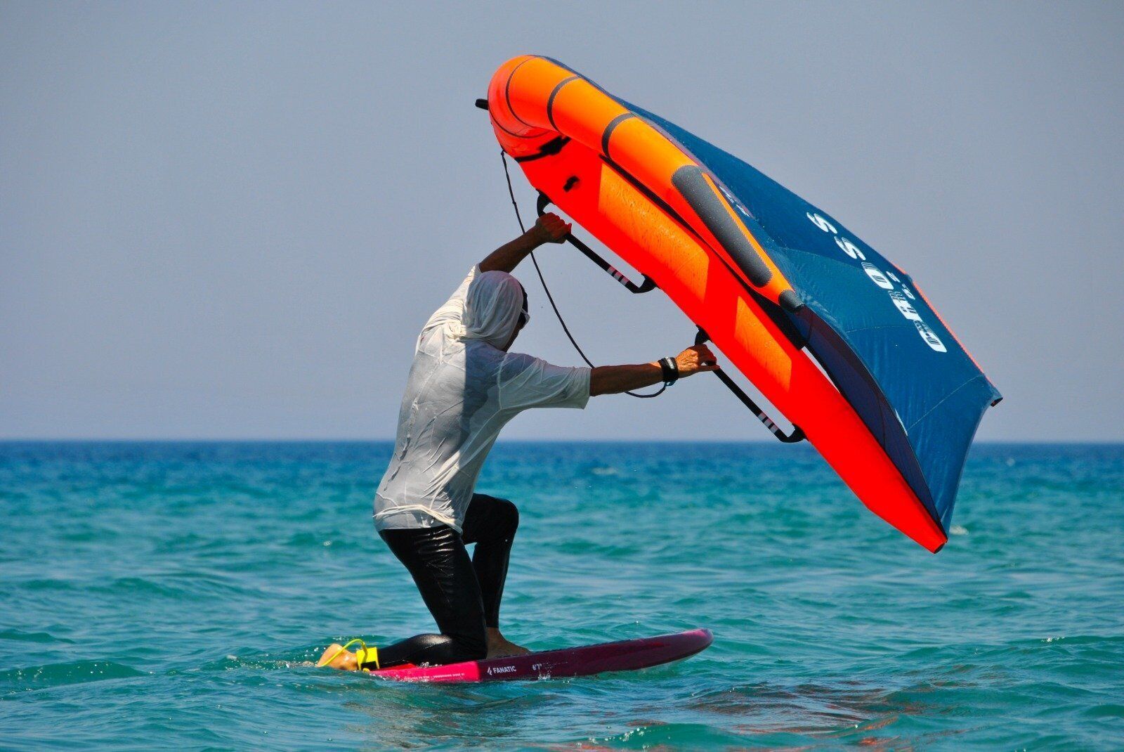 A person windsurfing with a large sail on a surfboard in the ocean.