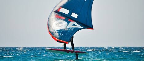 Eine Person windsurft bei klarem Wetter. Das Segel trägt die Aufschrift 'Cross 62'.