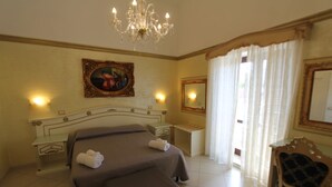 Ein Hotelzimmer mit einem großen Bett, einem Sessel, einem Schreibtisch, einer Chandelier, einem Gemälde und einem Spiegel.