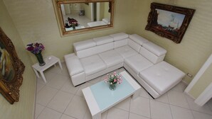 Ein Wohnzimmer mit einem weißen Ecksofa, einem Couchtisch mit Blumenvase, einem Spiegel und einem gerahmten Bild an der Wand.