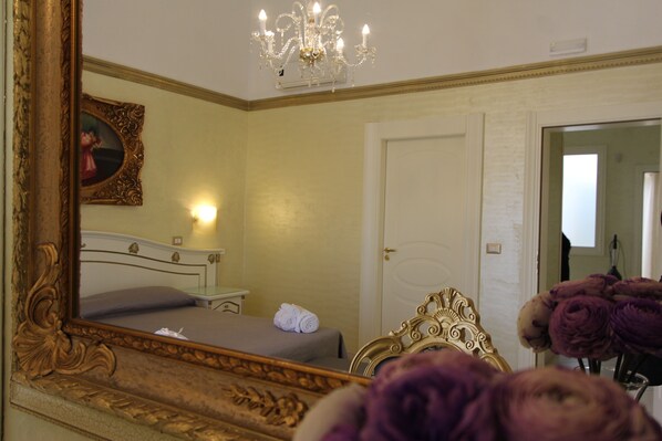 A hotel room with a large ornate mirror, a bed with a grey bedspread, a bedside table with a lamp, and a chandelier. - DIO DEL MARE LUXURY ROOM (Porto Cesareo)