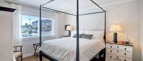 A four-poster bed with a white bedspread, a bedside table with a lamp, and a chair.