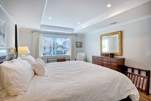 A neatly arranged bedroom with a large bed, a dresser, a mirror, and a window with curtains.