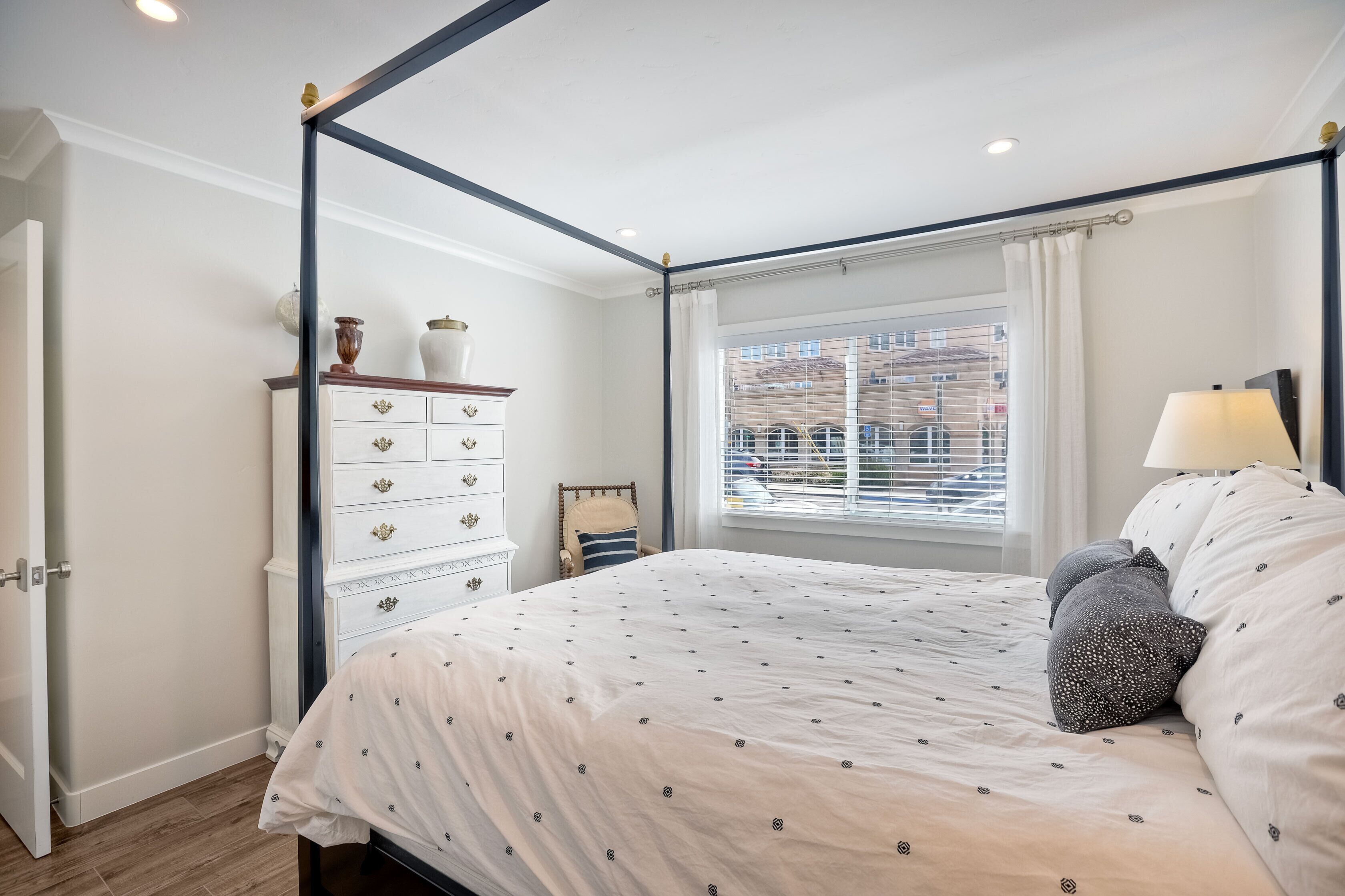 A four-poster bed with a patterned bedspread, a bedside table with a lamp, and a dresser with decorative items.