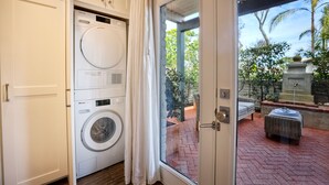 A laundry room with a front-loading washer and dryer, a glass door leading to an outdoor patio with a brick floor and outdoor furniture. - 90 Walk Score, Steps to Beach, Dining (Carlsbad)