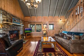 Ein Blockhaus-Interieur mit Kamin aus Stein, Ledersofa und Fernseher.