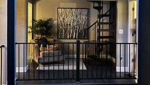 Een wooninterieur met twee verdiepingen, met een balkon, een trap en een zithoek met een bank en een plant.