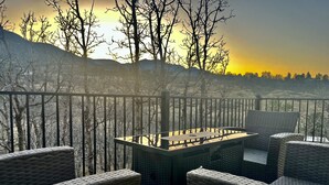 Een balkon met rieten meubilair en een tafel, met uitzicht op een bebost gebied in de achtergrond tijdens zonsondergang.
