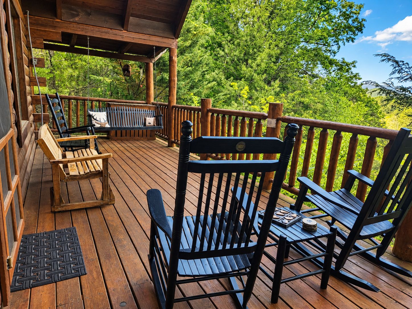 A wooden deck with a bench and chairs, a small table, and a doormat.
