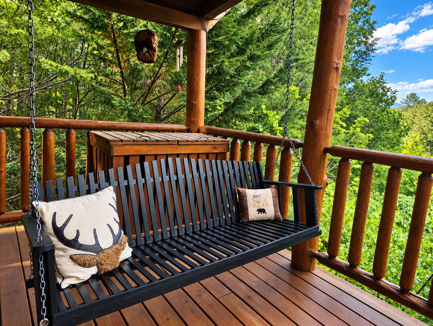 A wooden deck with a black metal swing bench and a cushion with a bear design.