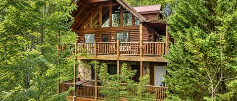 A cabin with a balcony, surrounded by dense forest.